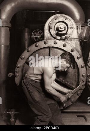 1920 , USA : ' Power house mechanic working on steam pump ' , photo taken by celebrated american photographer and sociologist LEWIS HINE ( 1874 - 1940 ) for the Work Progress Administration of US Govern. Hine used his camera as a tool for social reform.  This photo shows a working class American in an industrial setting. The carefully posed subject, a young man with wrench in hand, is hunched over, surrounded by the machinery that defines his job. But while constrained by the machinery (almost a metal womb), the man is straining against it —muscles taut, with a determined look in an iconic rep Stock Photo