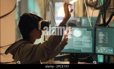 Male spy planting virus with vr headtset at night, using virtual reality to hack government database. Dangerous hacker doing cyber espionage on dark web, illegal harassment. Handheld shot. Stock Photo