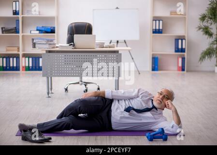 Old male employee doing sport exercises during break Stock Photo