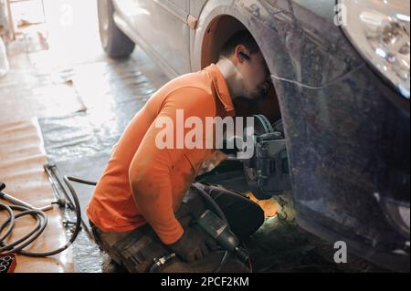 Mechanic man repairs the undercarriage of the car. A man repairs a car in a garage. Car wheel repair Stock Photo