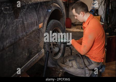 Mechanic man repairs the undercarriage of the car. A man repairs a car in a garage. Car wheel repair Stock Photo