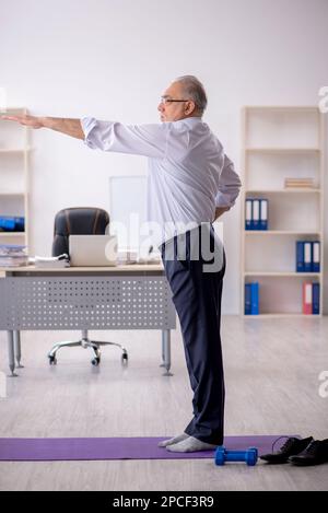 Old male employee doing sport exercises during break Stock Photo