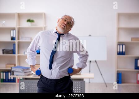 Old male employee doing sport exercises during break Stock Photo