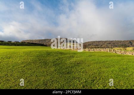 Lanscape of a green, grassy field below an old stone wall, hills, and dramatic sky in the Glens of Antrim, Northern Ireland Stock Photo
