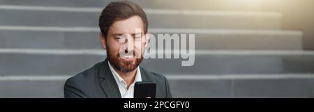 Smiling office worker in suit sitting on stairs with coffee during break and using phone Stock Photo