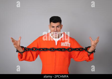 Emotional prisoner in orange jumpsuit with chained hands on grey background Stock Photo