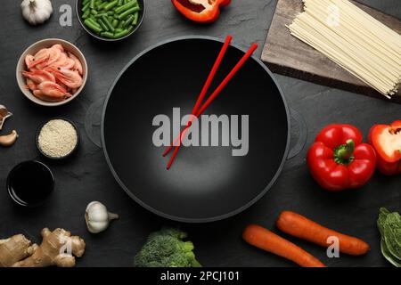 Empty iron wok with chopsticks and raw ingredients on black table, flat lay Stock Photo