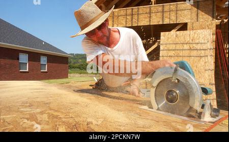 Rory Harville uses a circular saw to cut a piece of sheeting for