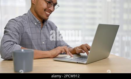 Cropped image of professional and smiling millennial Asian businessman using his laptop at his desk. Stock Photo