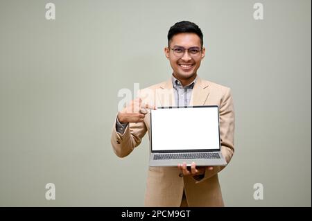 Happy and smiling adult Asian businessman in formal business suit holding his laptop, showing laptop blank screen, pointing his finger at laptop scree Stock Photo
