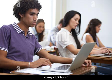 Focused on their assignments. a group of university students working on laptops in class. Stock Photo