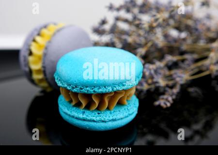 Monochrome gray macaron or macaroon on concrete background, almond cookies with different fillings chocolate, caramel sweet lavender macaroons French with flowers on black background, copy space Stock Photo