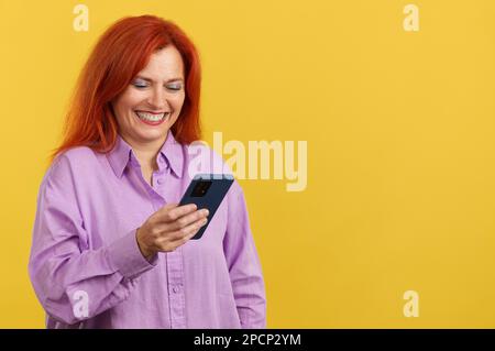 Happy mature redheaded woman smiling while using the mobile Stock Photo