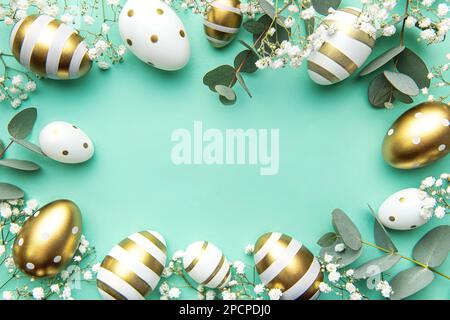 Easter eggs painted in gold and eucalyptus branches on a soft green background. Festive background Stock Photo