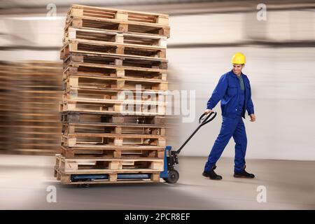 Worker moving wooden pallets with manual forklift in warehouse, back ...