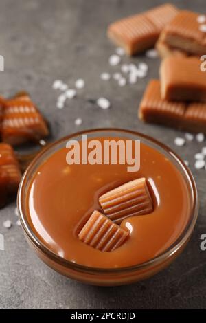 Tasty salted caramel with candies in glass bowl on grey table Stock Photo