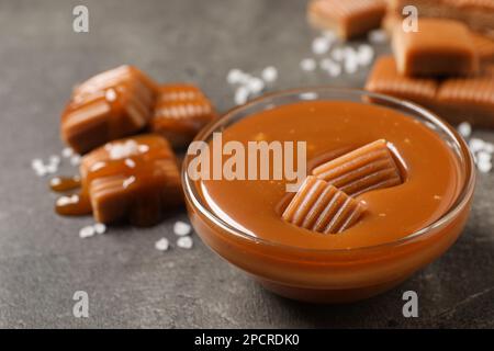 Tasty salted caramel with candies in glass bowl on grey table, closeup Stock Photo