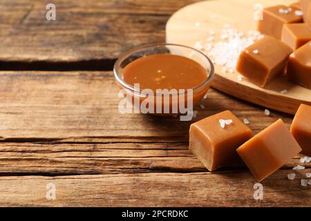 Yummy salted caramel in bowl and candies on wooden table, space for text Stock Photo