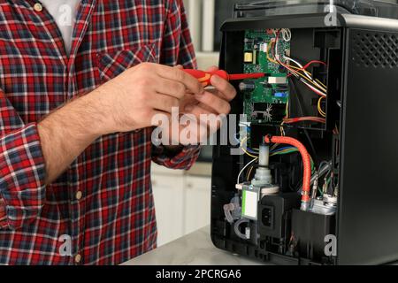 Man with screwdriver fixing coffee machine at table indoors, closeup Stock Photo