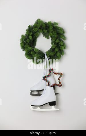 Pair of ice skates and Christmas wreath hanging on white wall Stock Photo