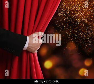Man opening red front curtain against blurred lights. Bokeh effect Stock Photo