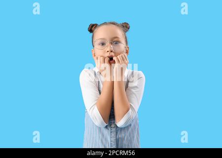Stressed little girl biting nails on blue background Stock Photo