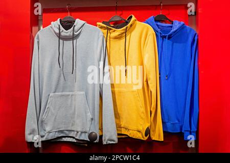 fashionable gray yellow blue hoodies hang on a hanger on a red background. Life style Stock Photo