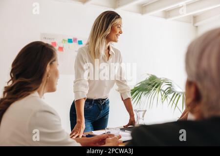 Cheerful young businesswoman having a meeting with her team. Team leader brainstorming with her colleagues in a boardroom. Group of creative businessw Stock Photo
