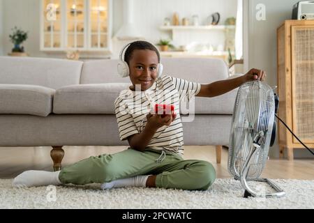 Smiling happy African American boy child relaxing at home in front of electric fan Stock Photo