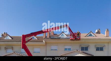 Workmen installing solar panels on the roof of a terraced house. They working over articulated boom lift Stock Photo