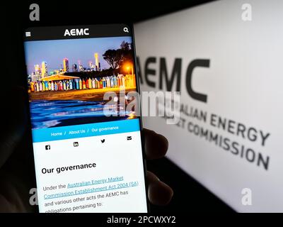 Person holding cellphone with website of Australian Energy Market Commission (AEMC) on screen in front of logo. Focus on center of phone display. Stock Photo