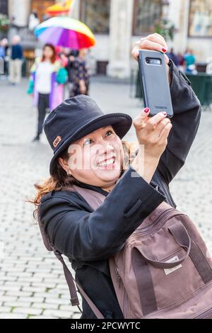 Lady on the Grand Place in Brussels, experiencing great joy in photographing the tower of the City Hall. Stock Photo