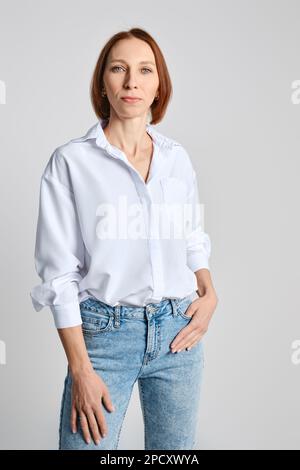 Portrait of confident middle aged woman posing against grey studio background Stock Photo