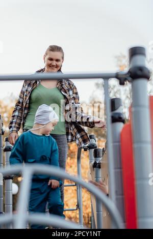 A boy, person with down syndrome walks in the park with his mother, going down the children's slide Stock Photo