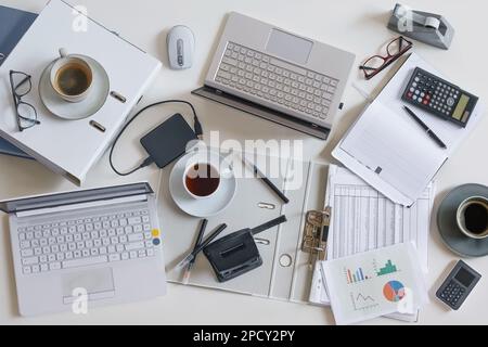 Top view of a full business desk with laptops, accounting papers, calculator, coffee and other office supplies, success work or stress concept, high a Stock Photo