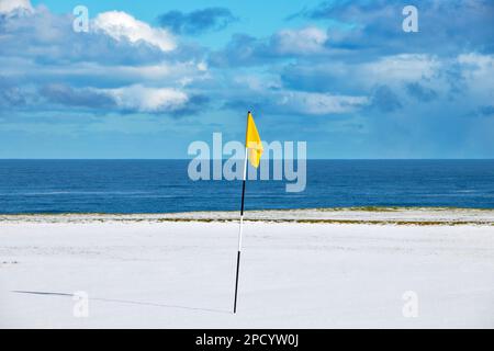 Cullen Bay Golf Course Moray Scotland blue sky over  the sea and a yellow flag on a snow covered green Stock Photo