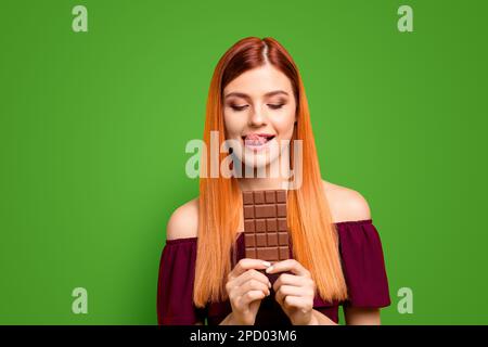 Young red-haired girl holding a chocolate bar isolated on yellow background Stock Photo