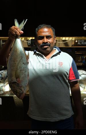 A vendor proudly holds up some fresh fish, catch of the day. At the fish market cooperative in Abu Dhabi, UAE, United Arab Emirates. Stock Photo