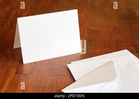 Standing blank empty rectangular greeting card and envelope mock up on dark wooden background with copy space. For use as a celebration template. Stock Photo