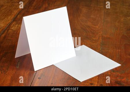 Standing blank empty square greeting card and envelope mock up on dark wooden background with copy space. For use as a celebration template. Stock Photo