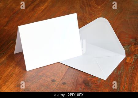 Standing blank empty rectangular greeting card and envelope mock up on dark wooden background with copy space. For use as a celebration template. Stock Photo