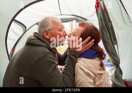 Loving elderly couple kissing on mouth while sitting in tent during camping at forest Stock Photo