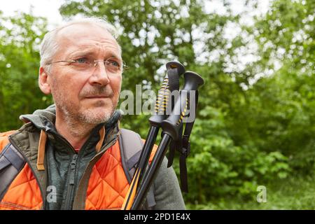 Thoughtful senior man in jacket with hiking poles looking away during vacation Stock Photo
