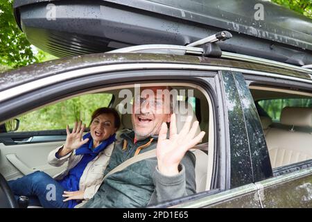 Portrait of happy senior couple waving hands while traveling in car during vacation Stock Photo