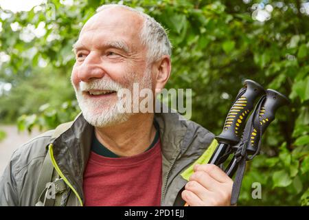 Smiling senior man with hiking poles in jacket looking away during vacation Stock Photo