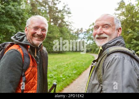 Portrait of happy elderly male friends carrying backpacks while hiking in forest during vacation Stock Photo
