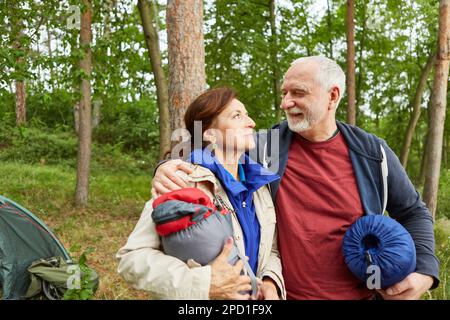 Smiling senior man with arm around woman holding tent in forest during vacation Stock Photo