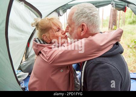 Senior couple kissing each other while sitting in camping tent during vacation Stock Photo