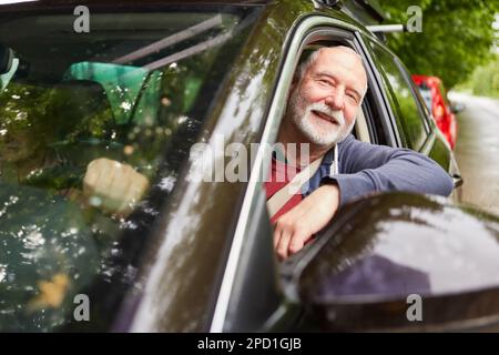 Portrait of smiling senior man looking through window while driving car during road trip Stock Photo