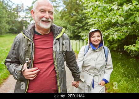 Portrait of cheerful elderly couple in jackets exploring forest during vacation Stock Photo